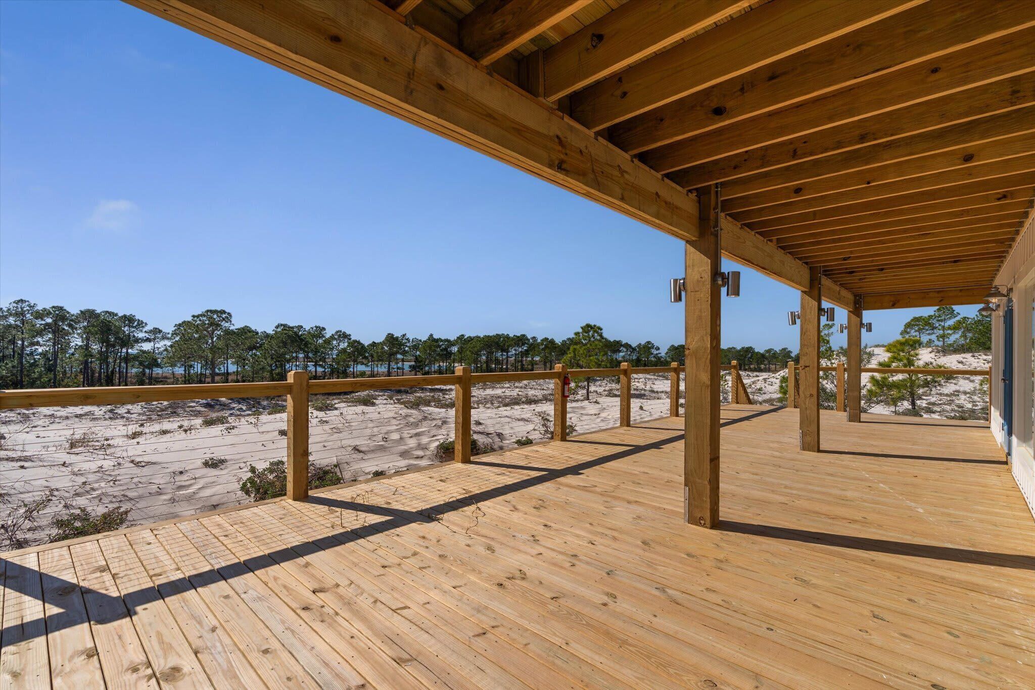 A wooden deck with a view of a sandy beach and trees.