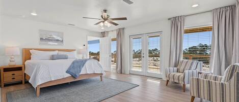 Un dormitorio con cama, mesita de noche, una silla, ventilador de techo y ventanas amplias.