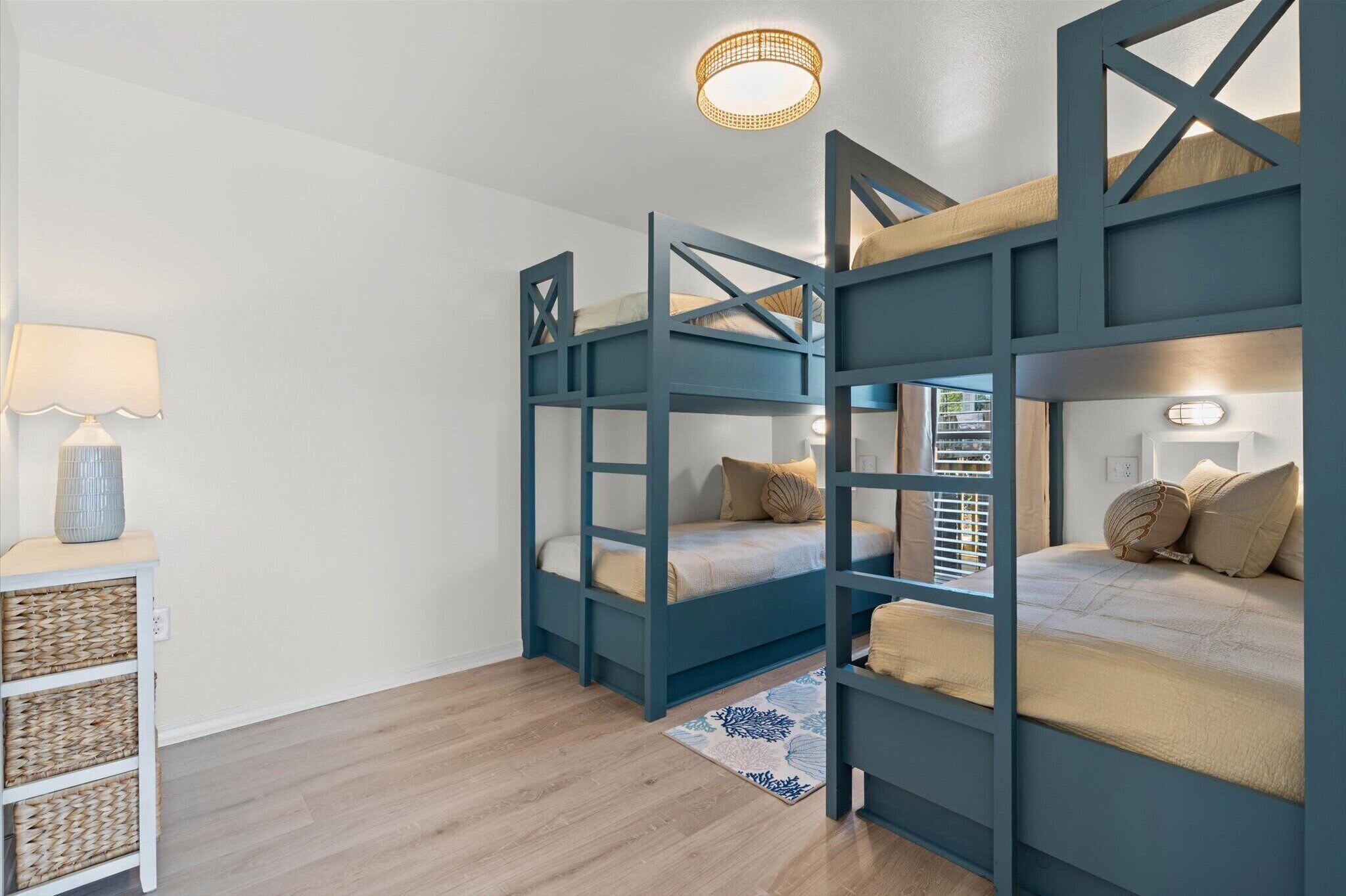 Ein Zimmer mit zwei Etagenbetten, einer weißen Wand, einem Holzboden, einer Lampe und einem kleinen Tisch mit Körben.