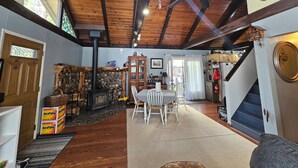 Una habitación acogedora con techo de madera, chimenea, una mesa de comedor con sillas y una escalera que sube a otro nivel.