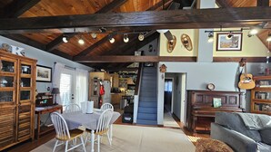Amplia sala de estar con una mesa de comedor, sillas, sofá y un reposapiés estampado. Una escalera conduce a un nivel superior.