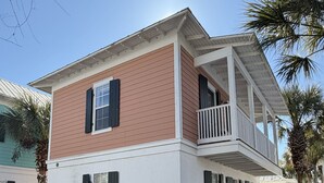 Uma casa de dois andares com varanda, rodeada por um deck de madeira e palmeiras.