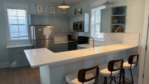 Uma cozinha moderna com armários azul claro, uma geladeira de aço inoxidável, micro-ondas e uma ilha grande com banquetas.