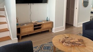 Sala de estar com televisão de tela plana, unidade de entretenimento em madeira, mesa de centro redonda e sofá azul.