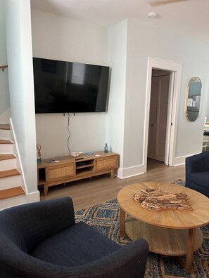 A living room with a flat-screen TV, a wooden entertainment unit, a round coffee table, and a blue sofa. - Beautiful 2-bedroom bungalow in enchanting Santa Rosa Beach with AC (Santa Rosa Beach)