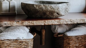 Ein Badezimmer mit einem Steinkonstruktion als Waschbecken, Holzkorben und einer Ziegelwand.