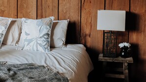 Ein Schlafzimmer mit Holzboden, einem Bett mit weißer Bettwäsche und einem Nachttisch mit Lampe und Blumenvase.