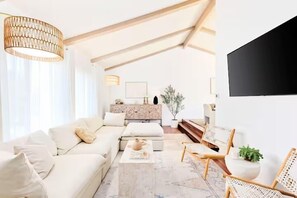 A spacious living room with a high ceiling, a sofa set, a coffee table, and a TV mounted on the wall. - Coastal Haven |King suite|5 min to beach|Garden (Del Mar)