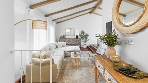 Un salon moderne avec un canapé, une table basse et une console en bois. Un grand miroir orne le mur, et un luminaire suspendu éclaire la pièce.