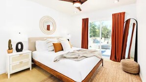 Une chambre moderne avec un lit en bois, une literie blanche, un ventilateur de plafond, une table de chevet avec une lampe et une vue sur l’extérieur.