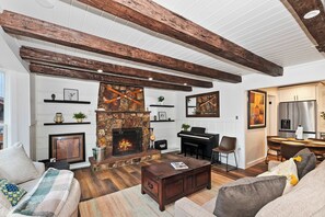 A living room with a fireplace, wooden beams, a piano, and a dining area. - Highland Cedar I Hot Tub + Fireplace I Village (Big Bear Lake)