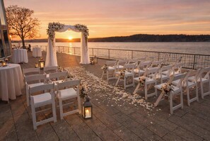 An outdoor wedding setup with white chairs and tables, a floral arch, and lanterns.