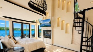 Un dormitorio con cama, televisión, chimenea, escalera y vista al agua.