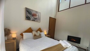 Un dormitorio ordenado con una cama grande, una mesita de noche con lámpara, un televisor montado en la pared y una puerta.