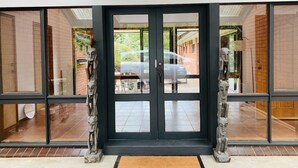 Una entrada de edificio moderna con una puerta negra, grandes ventanales de vidrio y piso de baldosas.