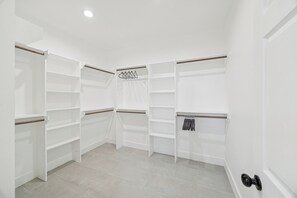 A walk-in closet with multiple shelves and hanging space, a ceiling light, and a door with a black handle. - Lone Star Getaway The Ultimate Texas Vacation Retreat (Houston)