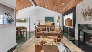 A spacious living room with a wooden ceiling, a large sofa, a coffee table, and a fireplace. - Desert Escape- Pool, Spa & Mountain Views (Palm Springs)