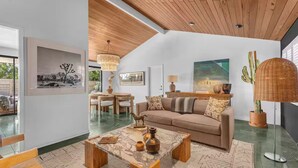 A spacious living room with a wooden ceiling, a beige sofa, a coffee table, and a cactus plant. - Desert Escape- Pool, Spa & Mountain Views (Palm Springs)