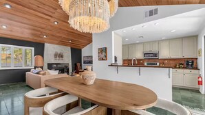 A modern living room with a wooden dining table, a large vase, and a chandelier. - Desert Escape- Pool, Spa & Mountain Views (Palm Springs)