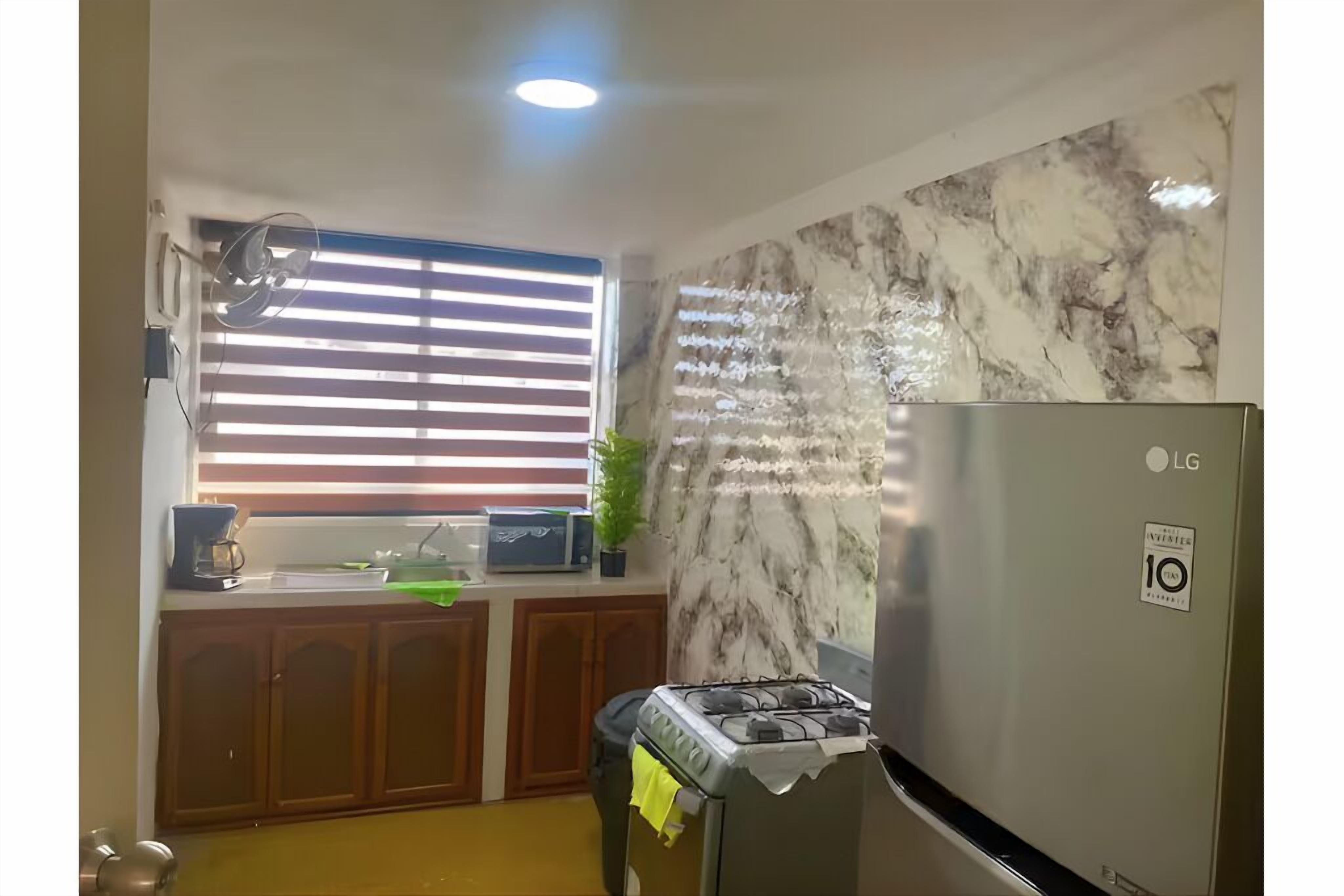 A kitchen with a gas stove, a refrigerator, wooden cabinets, a window with blinds, and a marble backsplash.