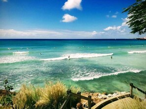 Ein Strand mit klarem türkisblauem Wasser, einer Holzpromenade und dichter Vegetation.