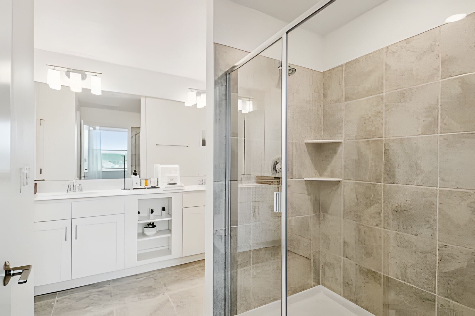 A modern bathroom with a glass shower enclosure, white cabinetry, and a large mirror with lights.