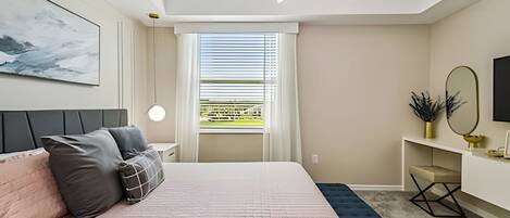 A modern bedroom with a large bed, a bedside table, a desk, a chair, a window with blinds, a ceiling light, and a wall-mounted mirror.
