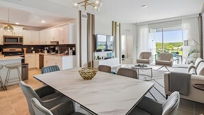 Een moderne keuken met witte kasten, een centraal eiland en een eethoek met een marmeren tafel.