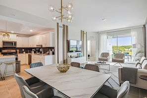 A modern kitchen with white cabinets, a central island, and a dining area with a marble table. - Luxury 3BR Condo Storey Lake Resort (Kissimmee)