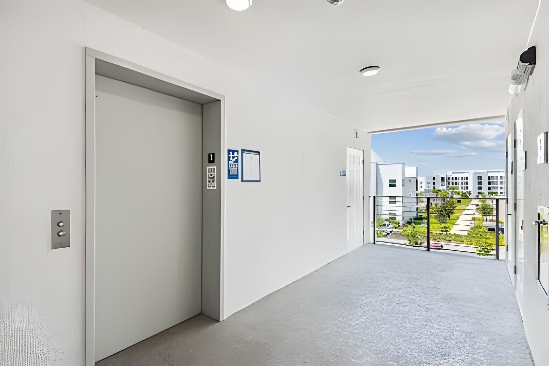A clean, modern hallway with a door on the left and a balcony with a view of buildings and greenery.