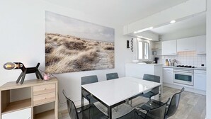Una cocina moderna con armarios blancos, una mesa de comedor con sillas y un cuadro abstracto grande en la pared.