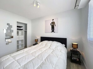 Ein Schlafzimmer mit Bett, Kleiderschrank, Nachttisch, Lampe und einem Wandbild.