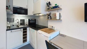 Eine kompakte Küche mit weißen Schränken, einer Mikrowelle, einem Toasterofen und einem Spülbecken. Über der Arbeitsfläche befinden sich Regale mit Küchenutensilien und einem Küchenpapierrollenhalter.