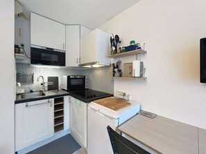 A compact kitchen with white cabinets, a microwave, a toaster oven, and a sink. There are shelves above the counter holding kitchen utensils and a roll of paper towels. - Quiberon - 2 rooms - 21m² - Close to the beaches (QUIBERON)