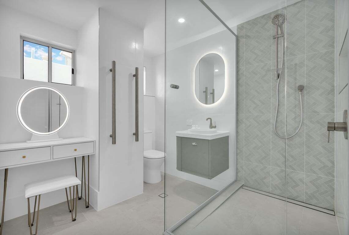 Een moderne badkamer met een wastafel, toilet, douche met glazen deur en een spiegel met verlichting.