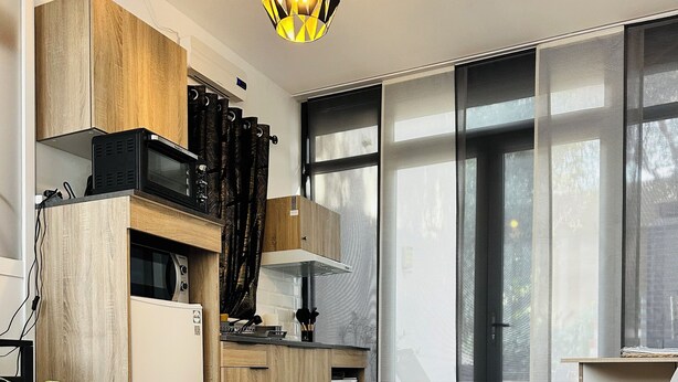 Un dormitorio moderno con una cama grande, una kitchenette con microondas y una ventana con persianas.