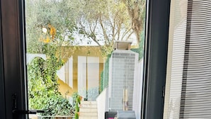 Vista a través de una puerta que muestra un patio con una parrilla, mobiliario exterior y una escalera que lleva a un área techada.