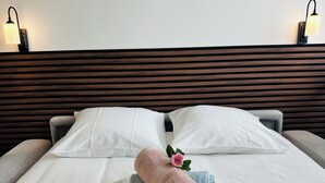 Una cama bien tendida con sábanas blancas, un cabecero de madera y dos lámparas fijadas a la pared.