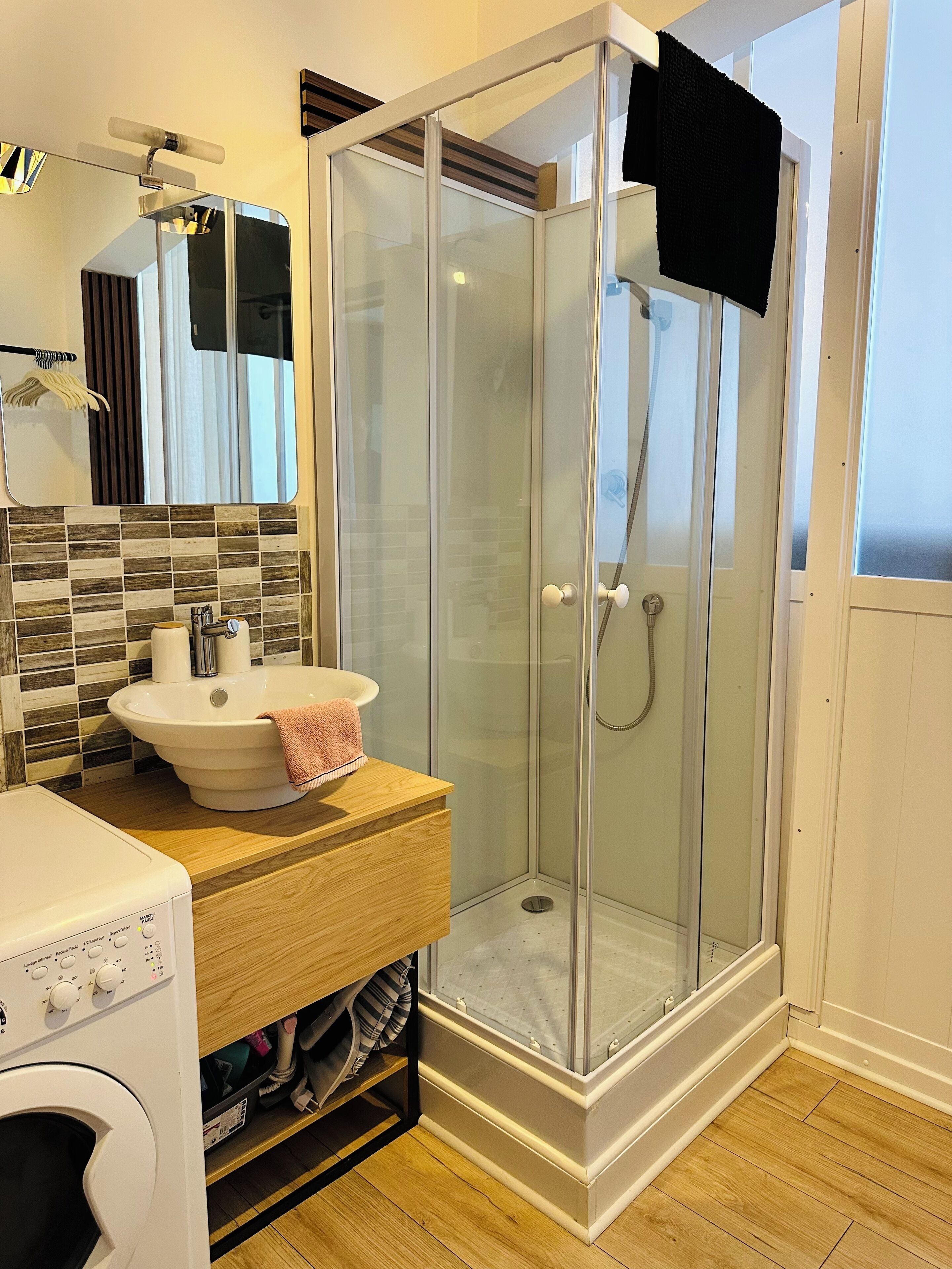 A modern bathroom with a glass-enclosed shower, a sink with a towel, and a washing machine.