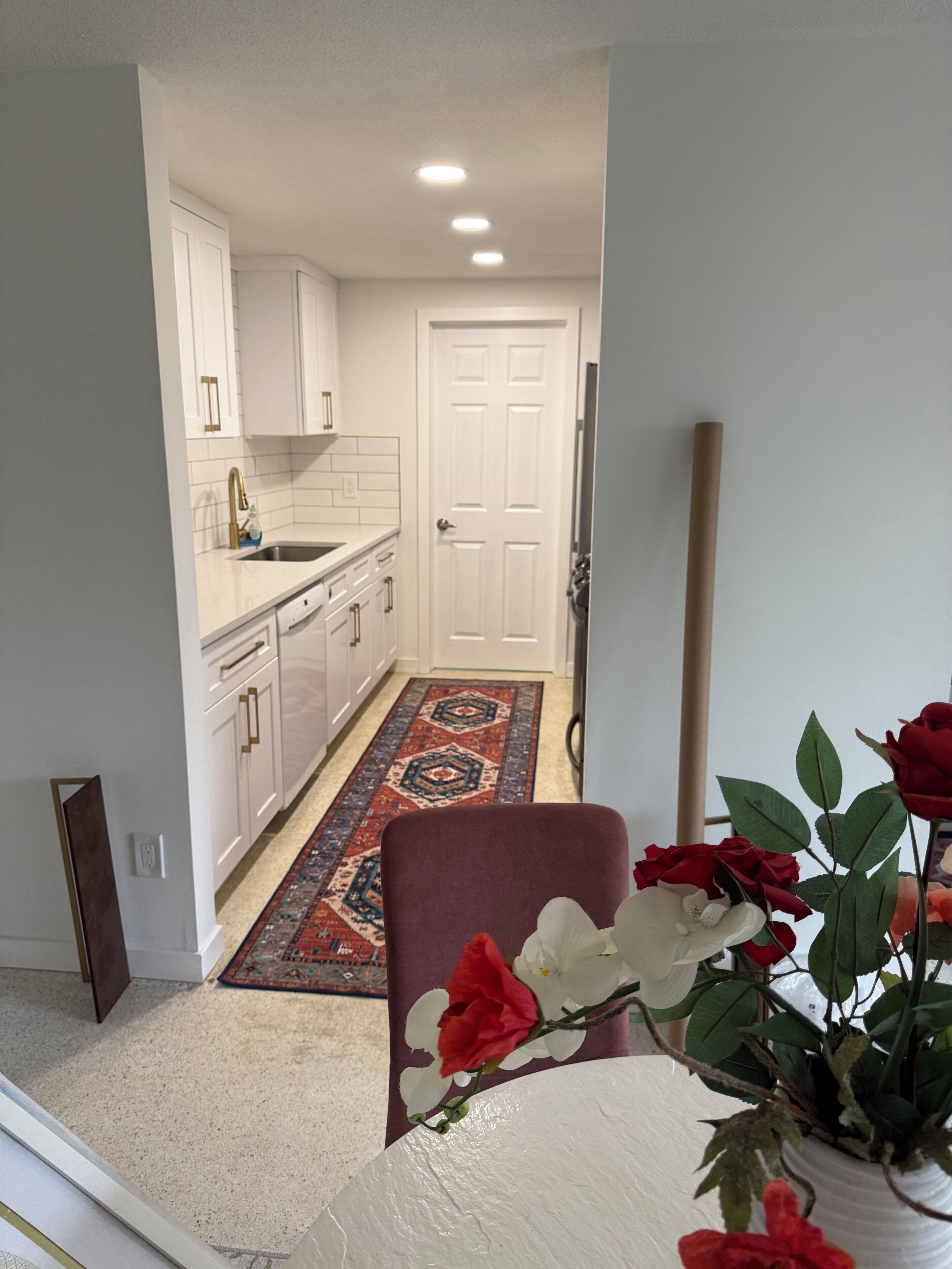 A kitchen with white cabinets, a sink, and a red rug leading to a door.