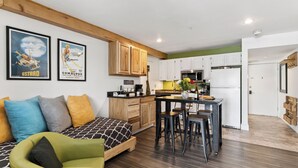 A modern kitchen with wooden cabinets, a dining area with stools, and a sofa with patterned cushions. - Blue Mesa Lodge 20B by Avantstay Prime Ski Access Condo Steps to Gondola, Lifts, & Dining (Telluride)