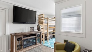 A living room with a TV mounted on the wall, a wooden entertainment unit, a sofa, and a window with blinds. - Blue Mesa Lodge 20B by Avantstay Prime Ski Access Condo Steps to Gondola, Lifts, & Dining (Telluride)