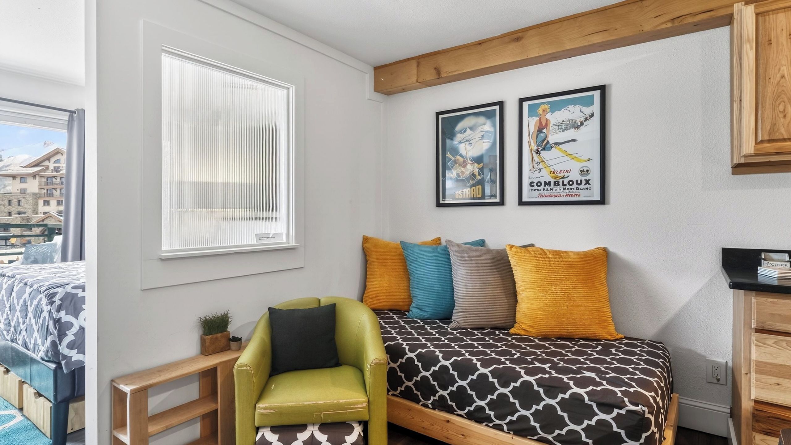 A bedroom with a bed, a green armchair, a window, and two framed posters on the wall.