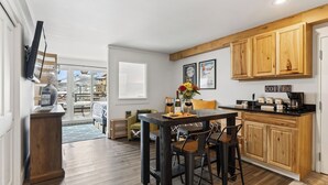 A kitchen with wooden cabinets, a dining table with chairs, a coffee station, and a view of a balcony with a chair. - Blue Mesa Lodge 20B by Avantstay Prime Ski Access Condo Steps to Gondola, Lifts, & Dining (Telluride)