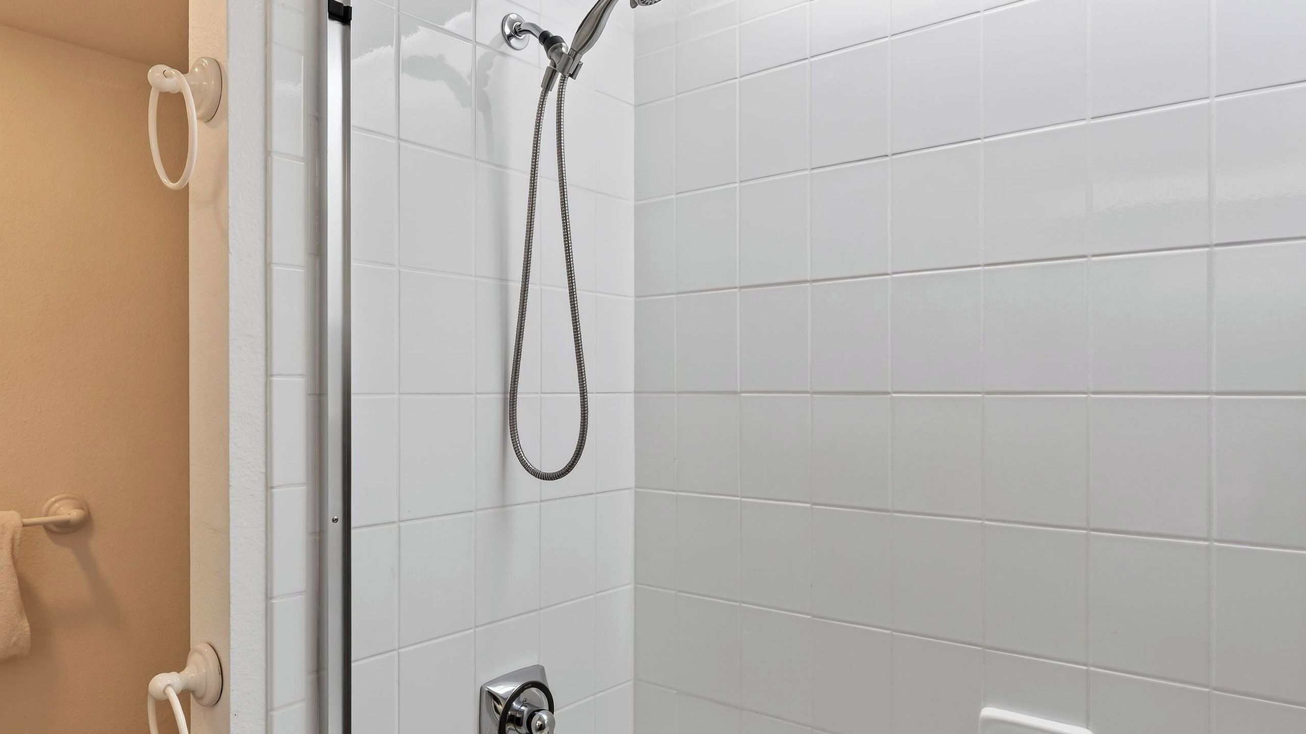 A shower with a handheld showerhead and a wall-mounted faucet, white tiled walls, and a towel rack.