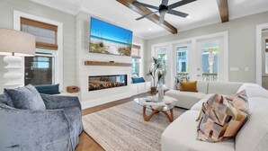 A modern living room with a fireplace, a ceiling fan, and a large painting of a beach scene. - Prescription for Paradise by Stay on 30a (Santa Rosa Beach)