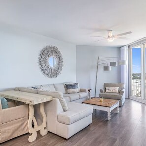 A living room with a sofa, coffee table, and armchair, a ceiling fan, and a large window with a view. - Gulf View - Amazing Sunrises (Destin)