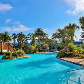 Une piscine d’un bleu éclatant, entourée de palmiers et bordée d’une terrasse en bois.