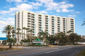 A multi-story hotel with a modern design, featuring balconies on each floor, surrounded by palm trees and a clear sky. - Gulf View - Amazing Sunrises (Destin)