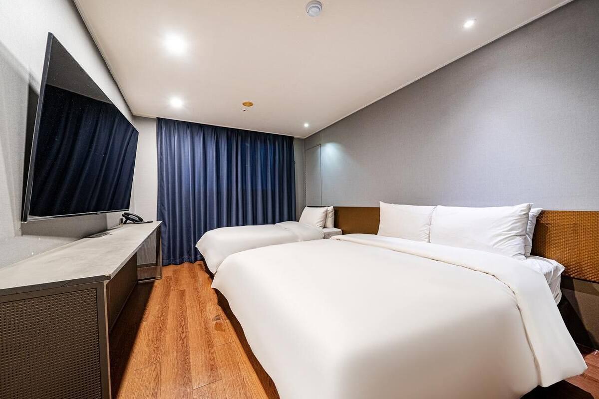 A hotel room with a bed, a desk, a mirror, and a window with curtains.